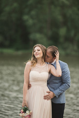 Fototapeta na wymiar Beautiful wedding couple, bride,groom kissing and posing on the bridge near lake