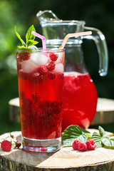 Homemade berry juice in a glass and jug with raspberry  redcurrant in  summer garden