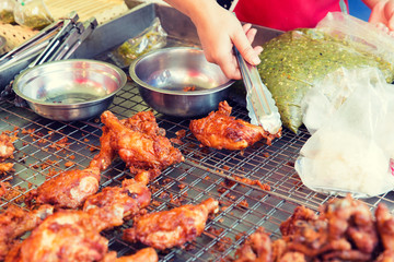 close up of cook hand with tongs grilling chicken