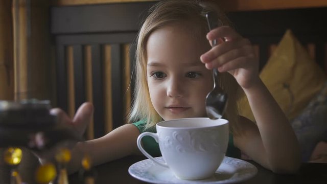 A little kid having breakfast at a cozy cafe. An adorable girl drinking tea and enjoying her breakfast.