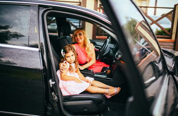 Fototapeta na wymiar Cute mother and her daughter are traveling by car. They are sitting on back seat and smiling. The girl is looking through window happily