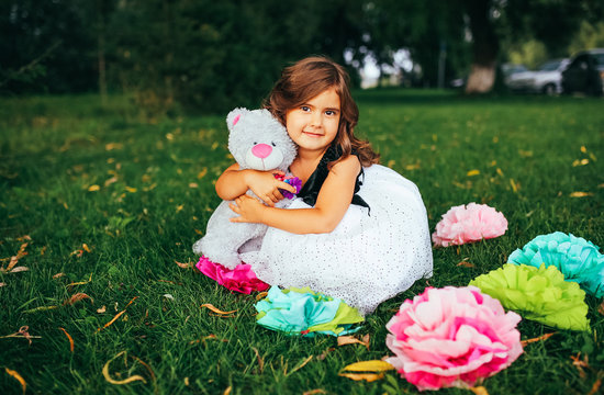Pretty girl playing with soft toy outdoor, cute infant having fun on backyard in spring time, happy childhood concept. Little girl in dress.