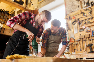 carpenters with drill drilling plank at workshop