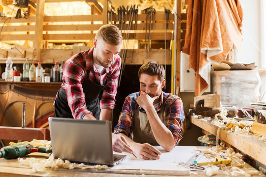 carpenters with laptop and blueprint at workshop