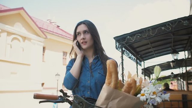 Beautiful girl standing in the street with a bike talking on the phone and smiling, slow mo