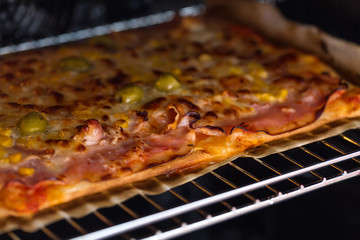 Homemade pizza with olive, ham, cheese and corn topping, baking