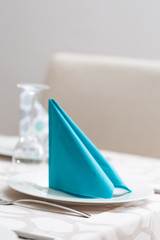 Detail of a served dinner table: white plate with fork; blue nap