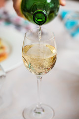 Man pouring white wine from the green bottle in a wine glass, on
