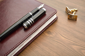 Business accessories on desktop: notebook, diary, fountain pen, cufflinks