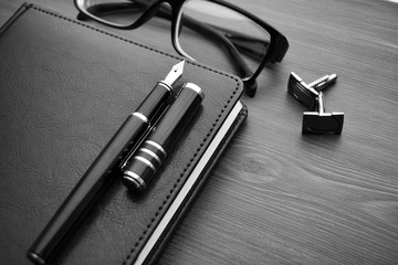 Business accessories on desktop: notebook, diary, fountain pen, cufflinks, glasses. 