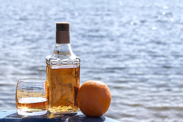 Bottle tequila and tumbler with Orange on the shore of lake
