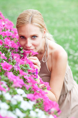 Fototapeta premium Beautiful blonde young woman smells flowers in a garden