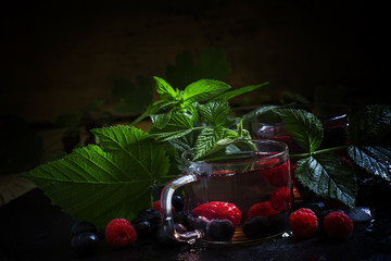 Summer berry drink with herbs, black background, selective focus