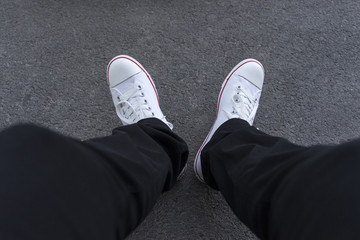 Men's feet in black trousers and white sneakers