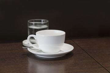 Cup of coffee with glass and water on wooden table