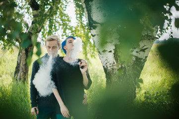 young couple with dyed hair smoking electronic cigarettes near birches. cloud head. cloud chasing