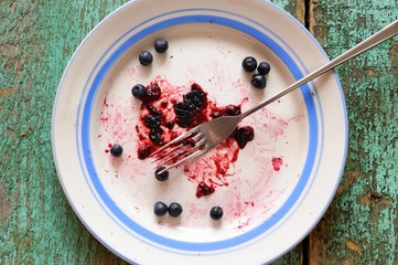 Dirty white plate with remnants of blueberry pie and several fresh blueberry