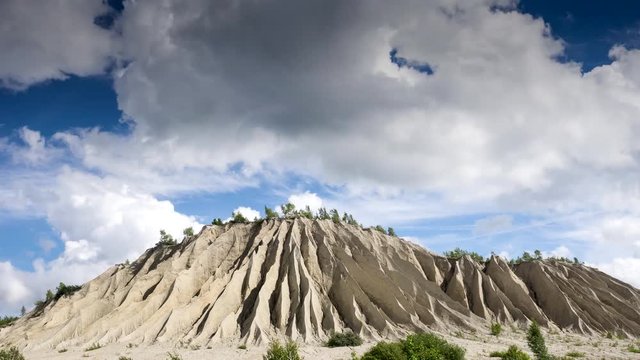 Old quarry mountain and moving white clouds over blue heaven. Abandoned mines and sky time lapse, 4K. The ashes dunes in Rummu. Estonia, Europe.