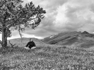 Woman sitting on a glade near the fir on the background of clouds