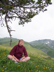 Pensive woman sitting under a branch on a background of mountains