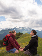 Naklejka premium Two young people sitting on the grass and holding hands on a background of mountains with clouds