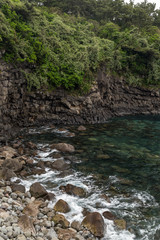 Rocky coastline and steep cliff next to Sojeongbang Falls on Jeju Island in South Korea.