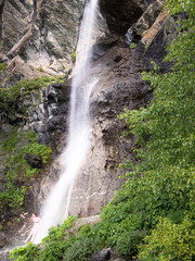 Woman in bathing suit standing under a waterfall in the background of mountains with trees