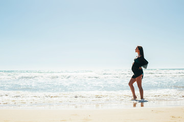 Silhouette of a pregnant woman on sea background. Expectant mother enjoys sea views. Beautiful pregnant woman standing on the beach