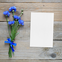 Bouquet of blue cornflowers and blank greeting card on wooden background