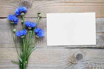 Cornflowers and blank card on wooden background