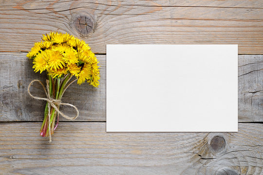 Bouquet of dandelion flowers and blank card on wooden background