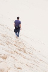 barefoot guy walking in the sand with his jeans in the beach