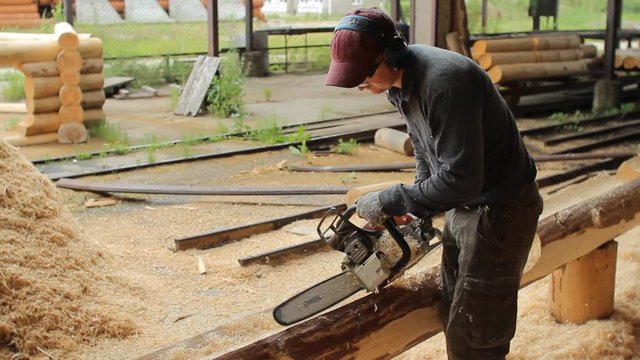 Man cuts off beam chainsaw for future home. Construction works with a wooden structure