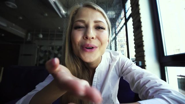 Young blonde woman showing hello gesture to somebody talking by internet, close-up