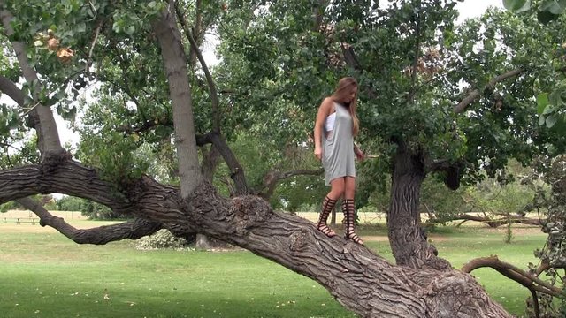 Attractive Caucasian Woman Standing On Tree In Gray Dress And Sandals

