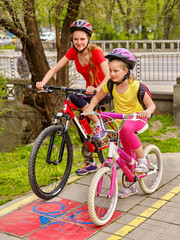Fototapeta premium Children girls wearing bicycle helmet with rucksack ciclyng bicycle. Girls children cycling on yellow bike lane. Bike share program save money and time. City trip.