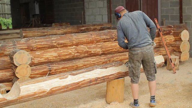 Man cuts off beam chainsaw for future log cabin. Construction works with a wooden structure