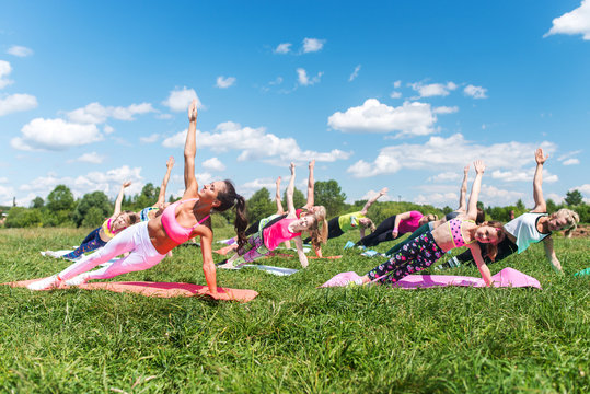 Group of fit girls going side plank exercise in nature on a sunny day.