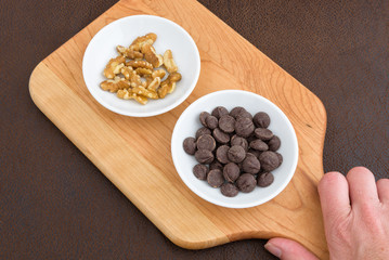 Hand holding cutting board with walnuts, and chocolate chips laid out to make a tasty treat
