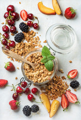 Healthy breakfast ingredients. Oat granola in glass jar with peach, strawberry, sweet cherries, blackberries on light marble background