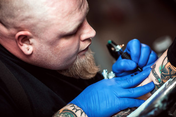 master tattooist makes a tattoo on the skin of the client in a workshop with special equipment