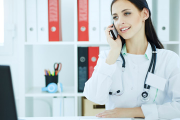 Portrait of a beautiful female medical doctor  talking on the phone and looking at the laptop.