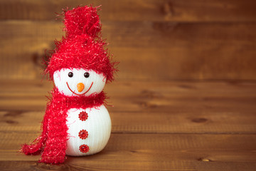 Knitted snowman in a red hat on wooden background