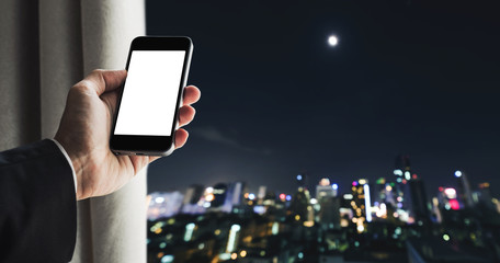 Businessman holding mobile phone with copy space on screen, and opening curtain defocus nightlife city view