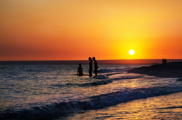 Silhouettes of people in the sea at sunset background
