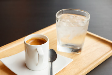 Cup of hot espresso coffee and glass of cold water on wooden tra