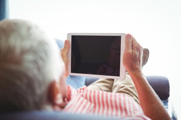 Lying on a couch senior man looking at digital tablet