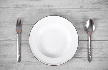 white plate, spoon and fork on old white wooden table