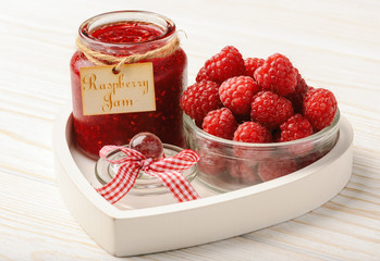 Raspberry jam in glass jar and raspberries.