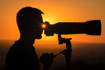 The man use the camera against the background of sunset